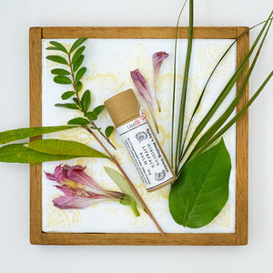 "Hibiscus Lip and Face Balm" tube in a wooden frame surrounded by leaves and flowers.
